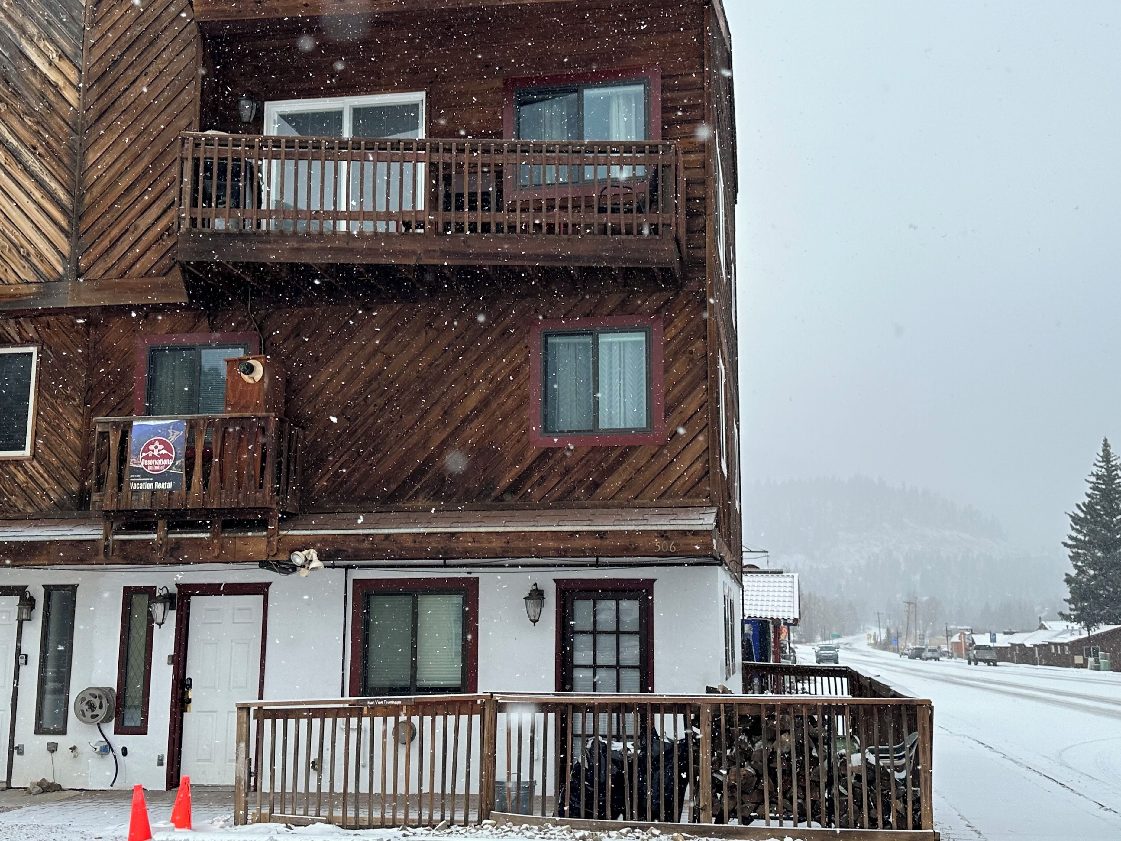 Un immeuble en bois à plusieurs étages, doté de balcons, avec une enseigne indiquant qu’il propose des locations de vacances, et un paysage enneigé.