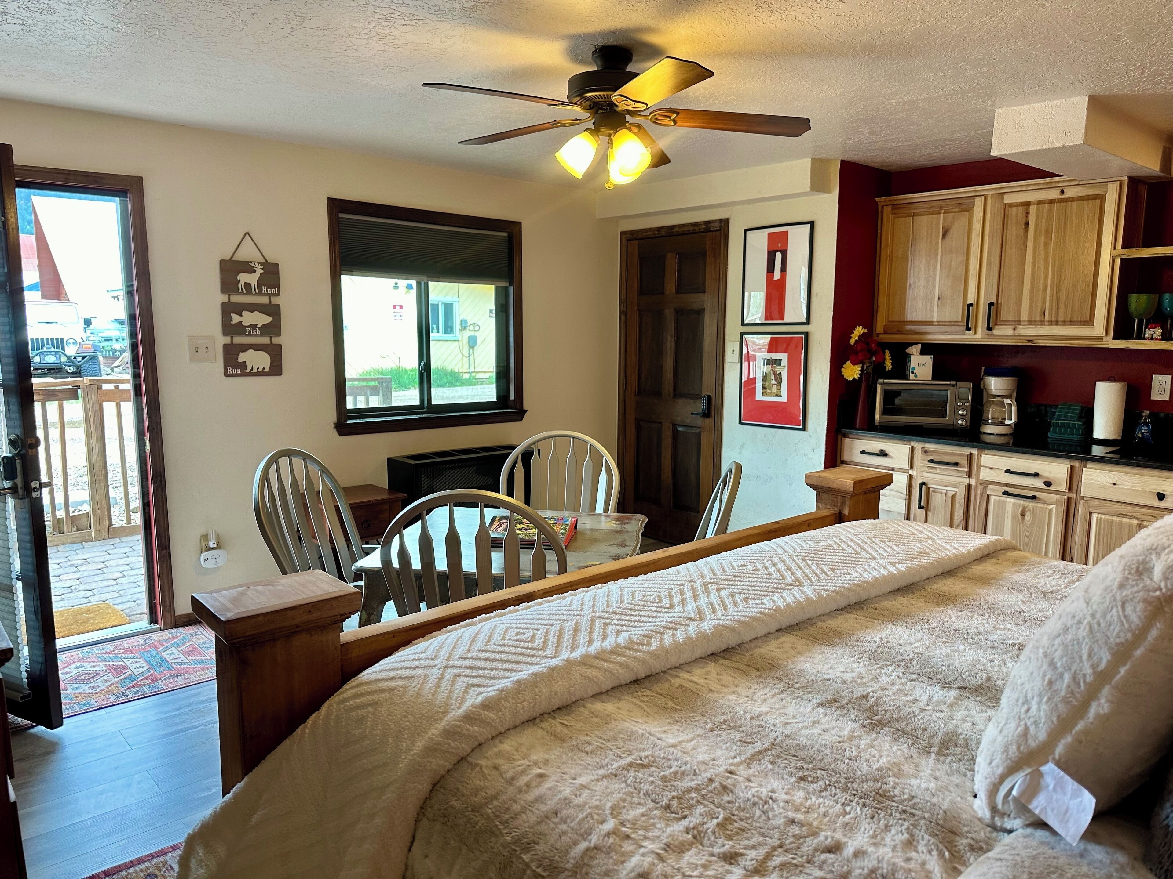 A cozy bedroom with a bed, a ceiling fan, a dining table with chairs, and a view of the outside through a window.