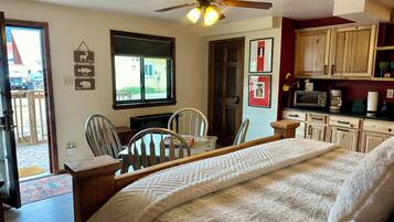 Une chambre confortable avec un lit, un ventilateur de plafond, une table à manger avec des chaises et une vue sur l’extérieur par une fenêtre.