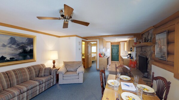 A cozy living room with a sofa, a dining table set for four, and a kitchen in the background. - 101 River - Full Property (Red River)