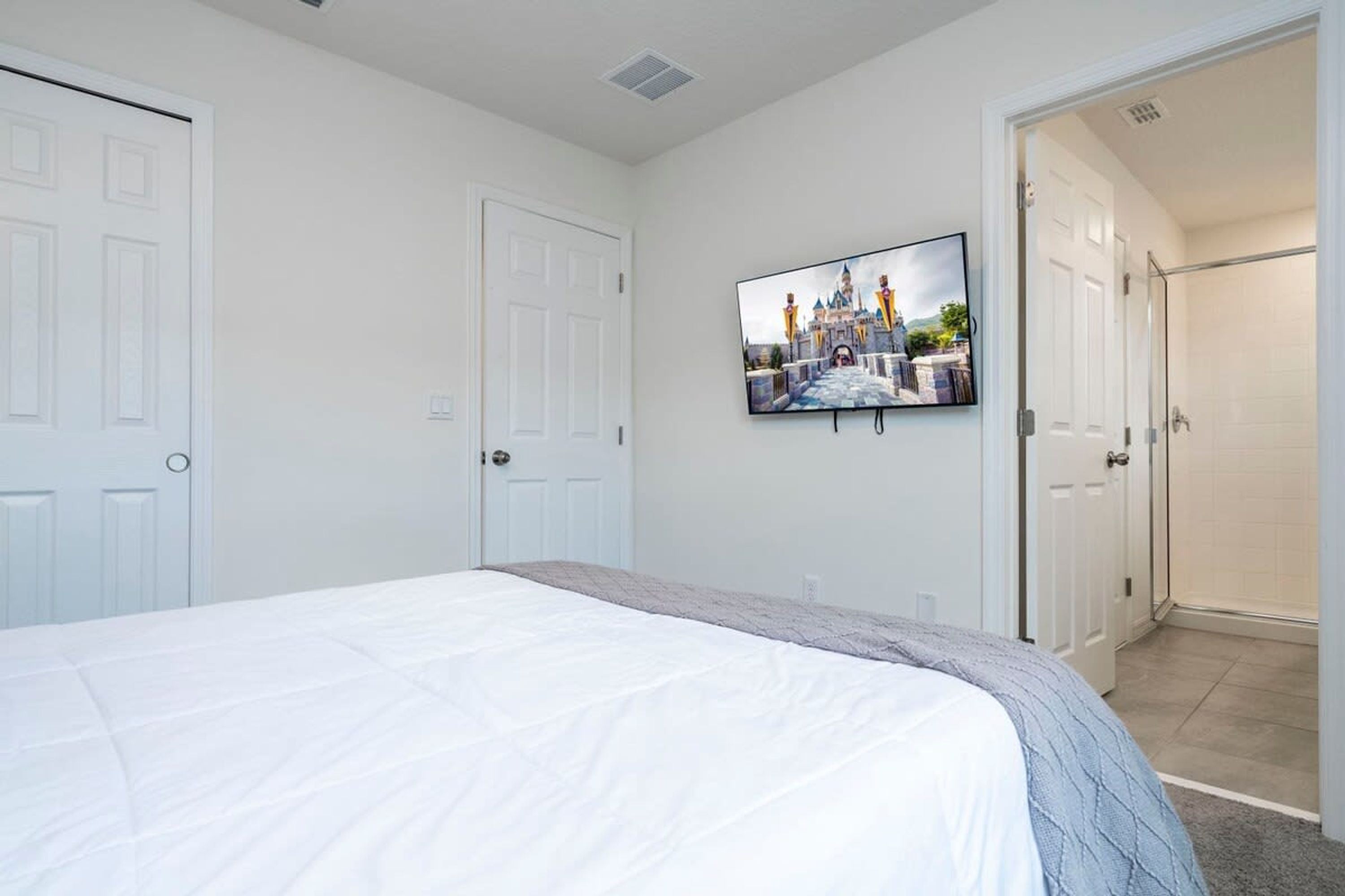 Une chambre à coucher avec un grand lit, un téléviseur fixé au mur et une porte donnant sur une salle de bain.