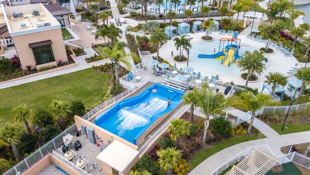 An aerial view of a resort with a central swimming pool, a water slide, and lounge areas surrounded by palm trees. - Splendid 5Bd w Pool at Solara Resort 2154 (Kissimmee)