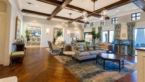 A spacious living room with a high ceiling, wooden beams, and a large window. There is a seating area with a sofa and chairs, a coffee table, and a TV. - Splendid 5Bd w Pool at Solara Resort 2154 (Kissimmee)