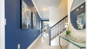 A hallway with blue walls, a glass console table, and a staircase with a black railing. - Fantastic 4 Bd w Pool at Storey Lake Resort 2709 (Kissimmee)
