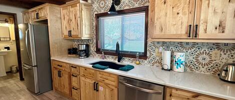 A kitchen with wooden cabinets, a stainless steel refrigerator, a dishwasher, and a window with blinds.