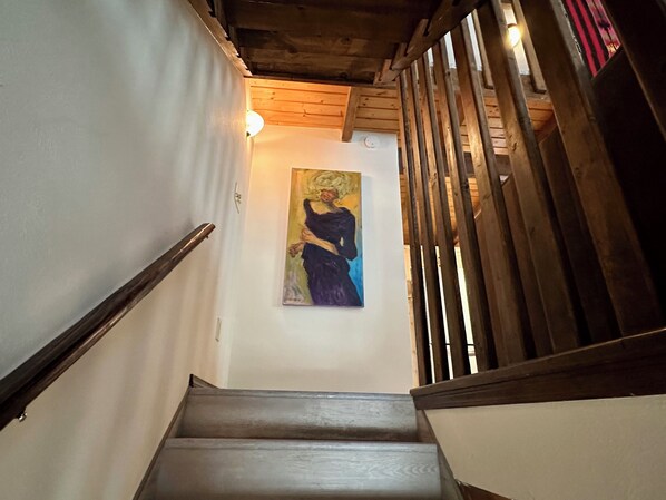 A wooden staircase with a handrail, a painting on the wall, and a light fixture above.