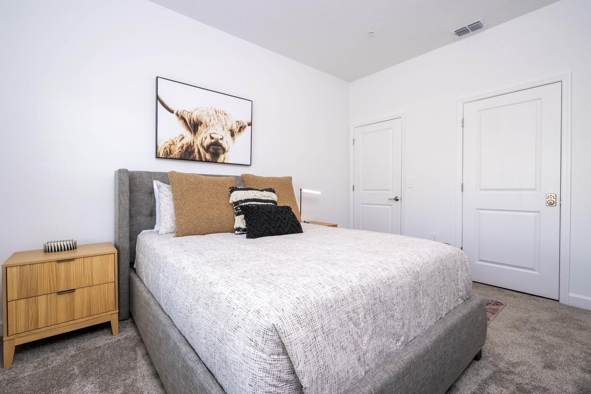 A bedroom with a bed, a nightstand, a framed picture, and two doors.