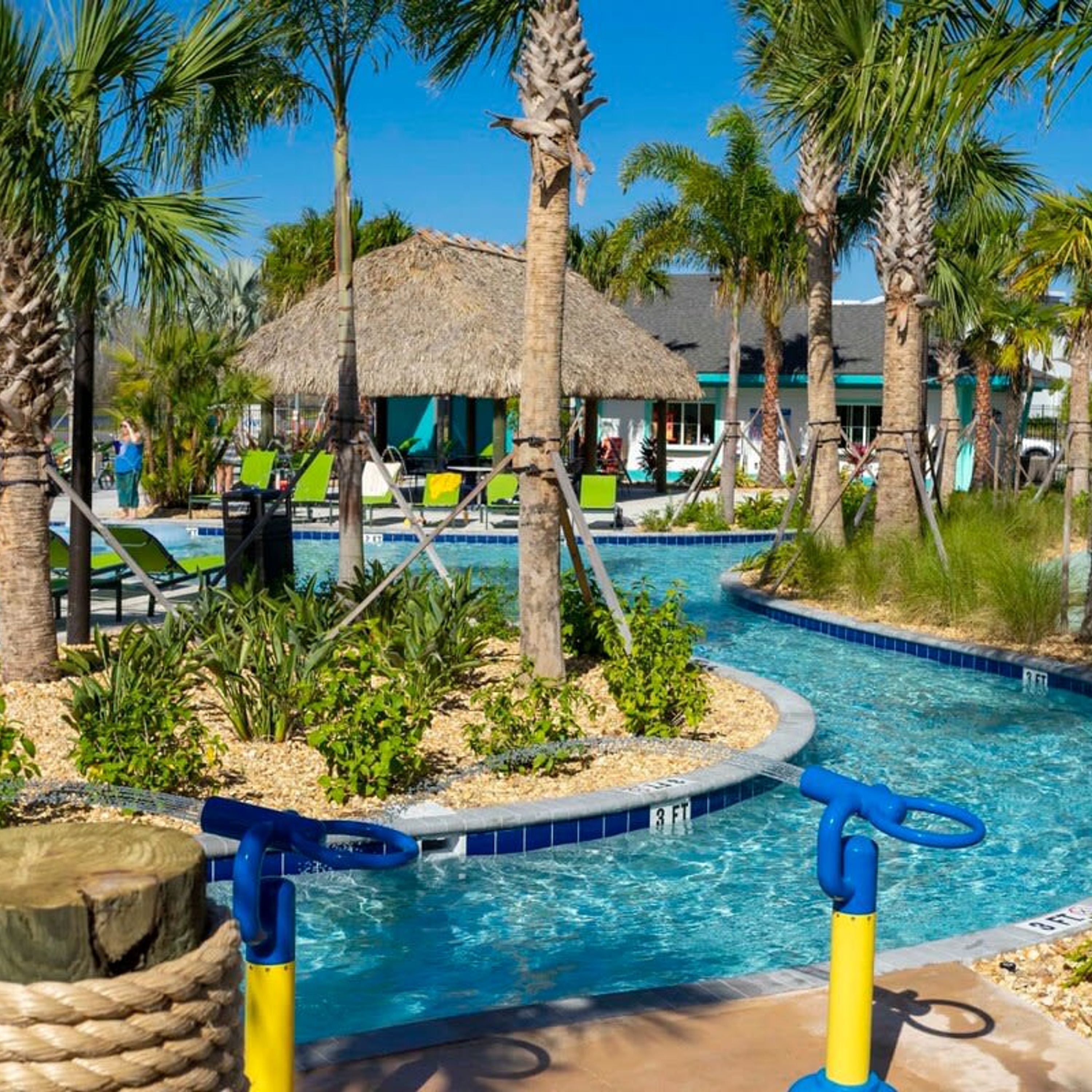 A pool area with palm trees, lounge chairs, and a thatched-roof structure.