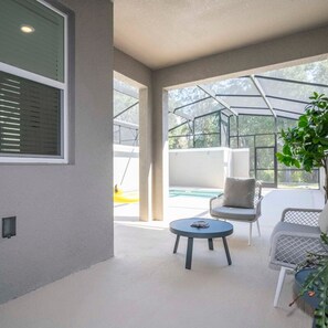 Un espace patio extérieur moderne, doté d’une table ronde et de deux chaises, d’une grande fenêtre et d’une vue sur une piscine.