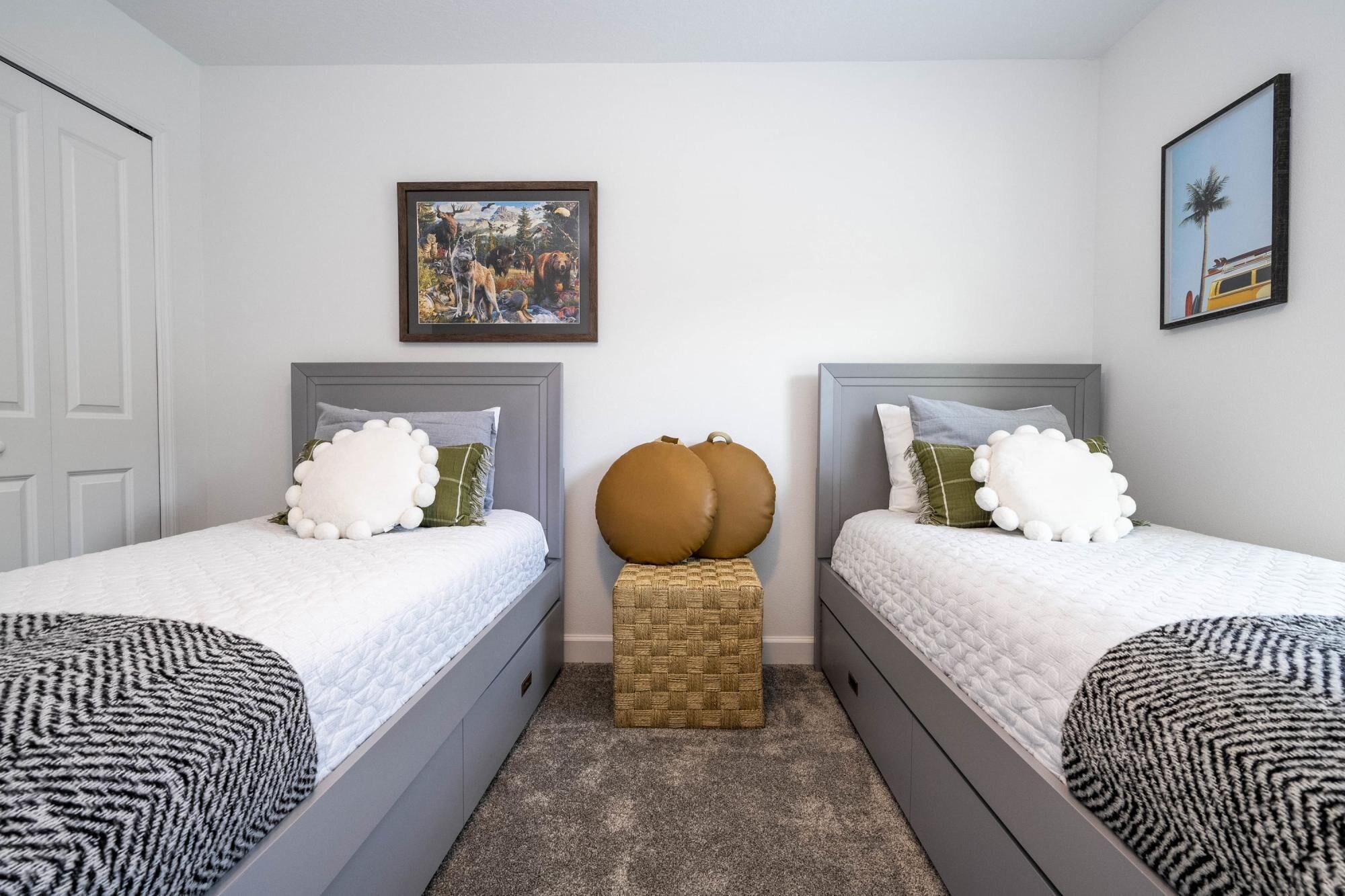 A bedroom with two beds, a woven stool, and two framed pictures on the wall.