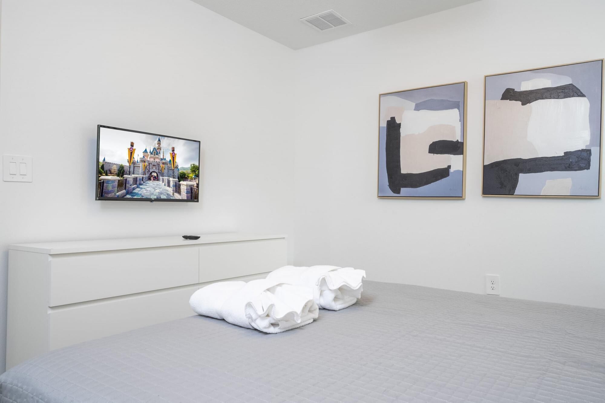 Una camera d'albergo con un letto, una TV a schermo piatto, un quadro astratto appeso al muro e un comodino bianco.