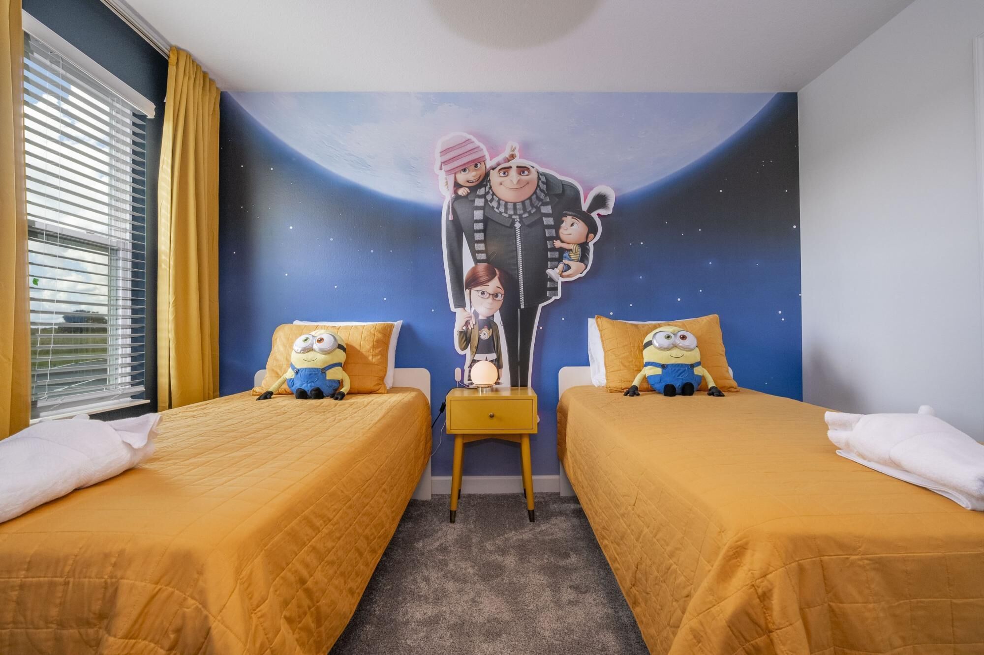 A bedroom with two beds, a mural of characters on the wall, and a window with curtains.