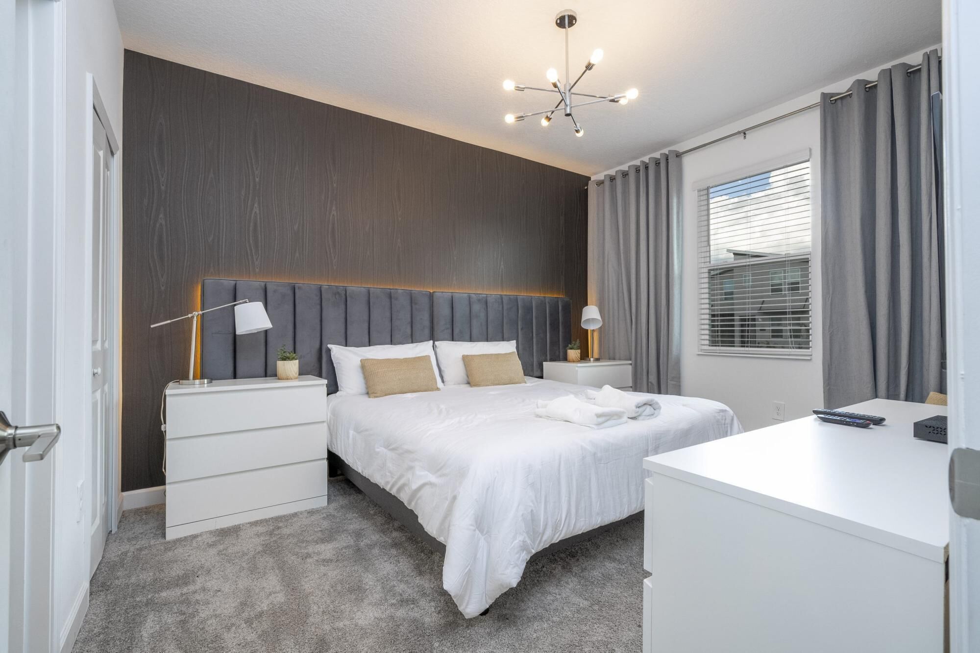 A modern hotel room with a large bed, bedside tables, a desk, and a ceiling light fixture.