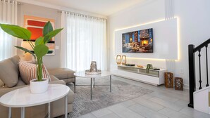A modern living room with a sofa, a coffee table, a potted plant, a TV mounted on the wall, and a staircase. - Free Waterpark 5Bd Close to Disney Private Pool (Kissimmee)