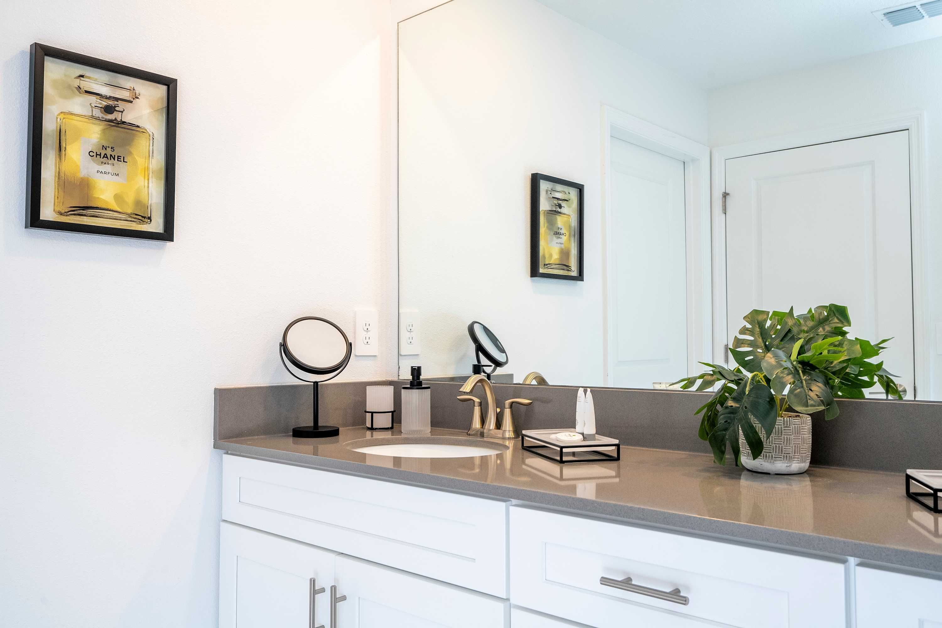 A modern bathroom with a large mirror, a sink, and a potted plant.