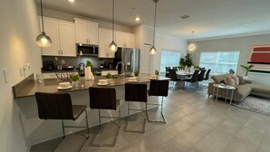 A modern kitchen with white cabinets, stainless steel appliances, and a central island with bar stools. - Free Waterpark 5Bd Close to Disney Private Pool (Kissimmee)