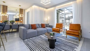 Una sala de estar moderna con un sofá gris, sillones naranjas, una mesa de centro y una zona de comedor con sillas y una mesa.