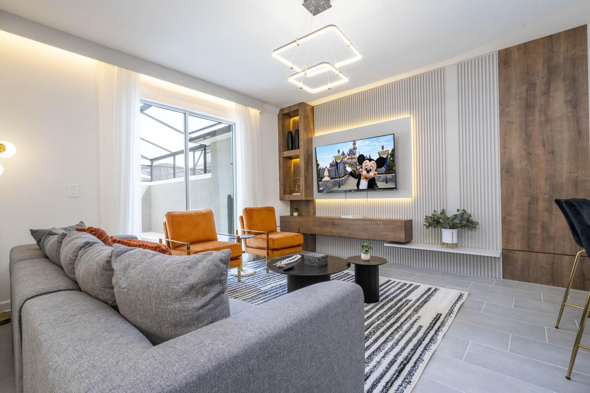 Una sala de estar moderna con un sofá gris, sillones naranjas, un televisor de pantalla plana y una pared de acento de madera.
