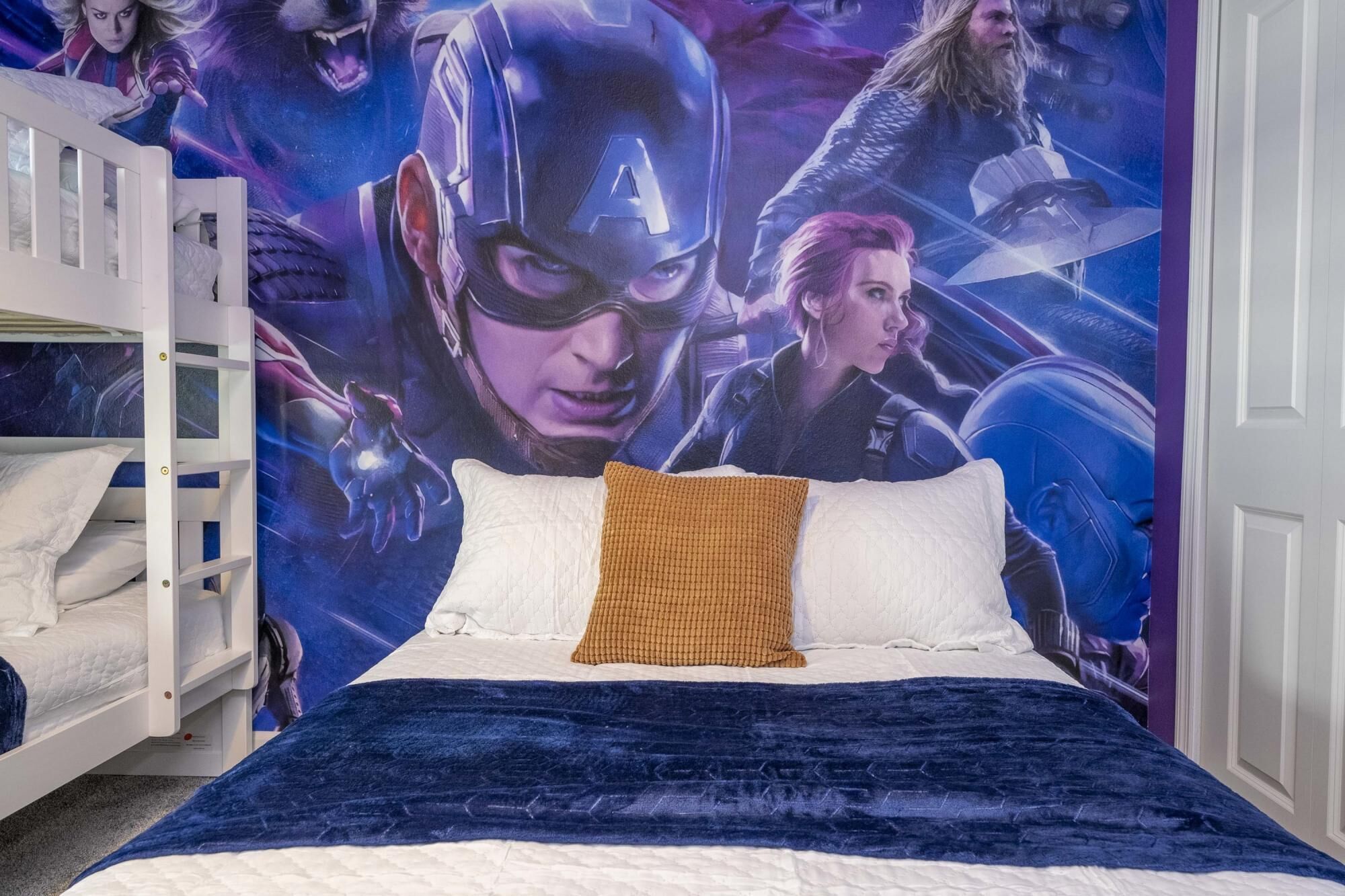 Une chambre avec un lit superposé, une grande fresque murale sur le thème des super-héros et une couverture de lit bleue.
