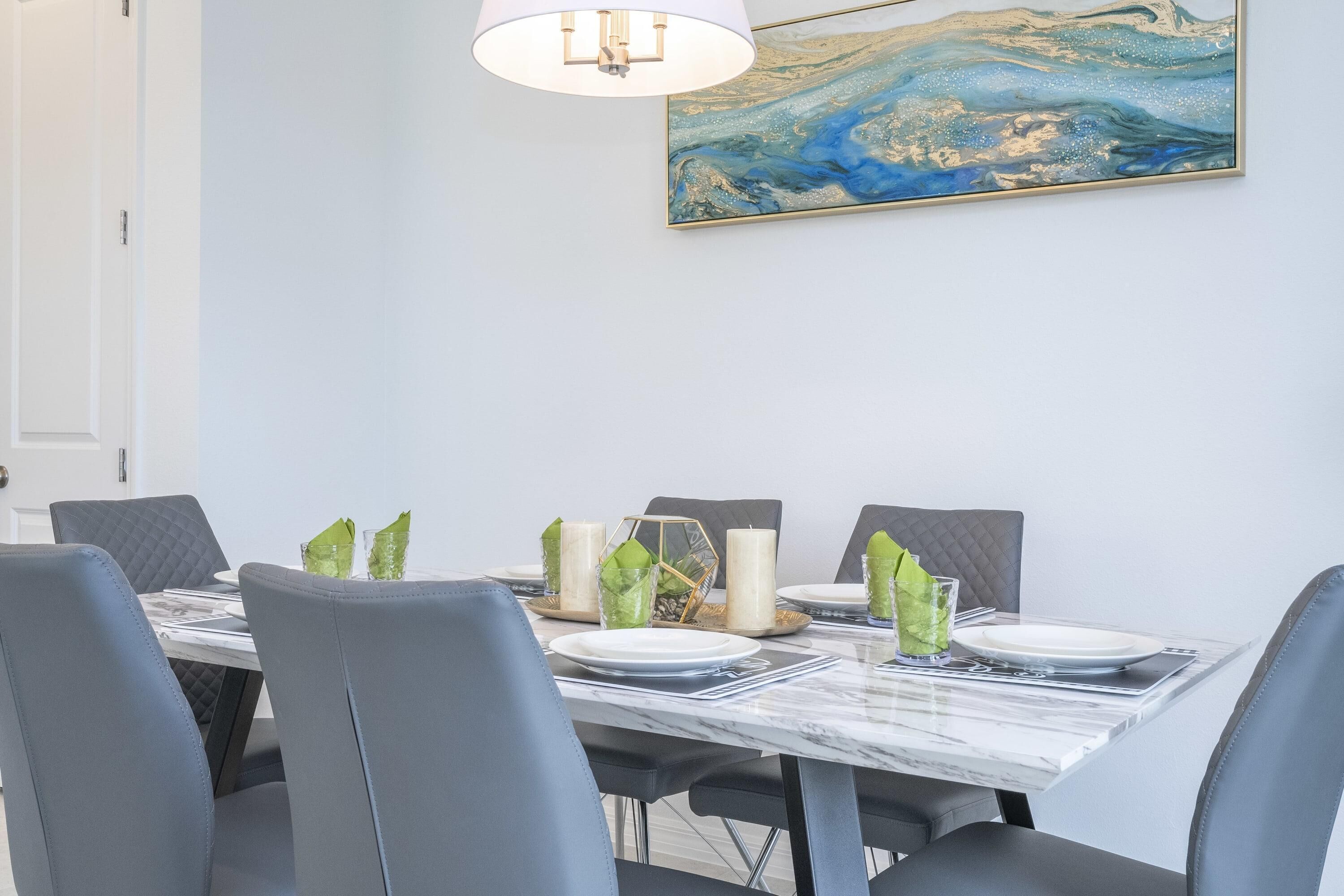 A dining area with a marble table, grey upholstered chairs, and a wall-mounted painting.