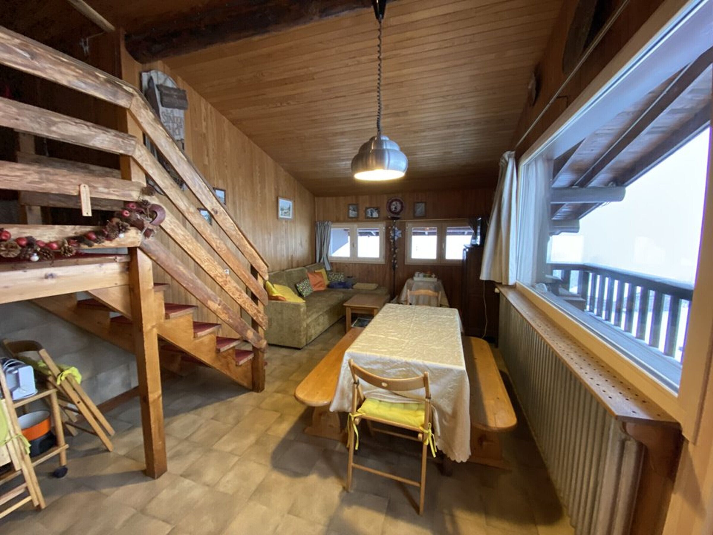 Et træhytteinteriør med spisebord, sofa, trappe og et stort vindue.