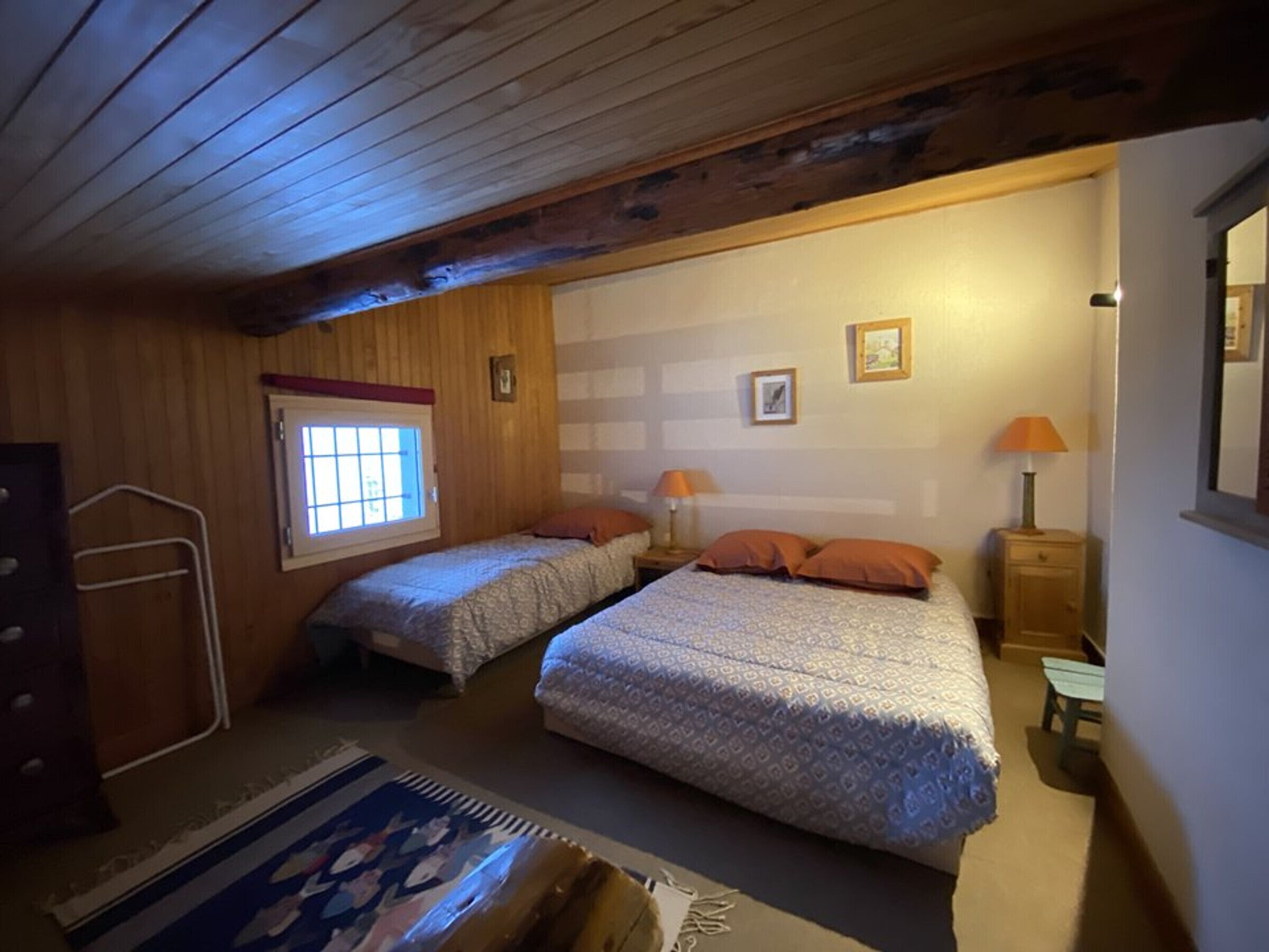 Ein gemütliches Schlafzimmer mit zwei Betten, einem Fenster und einem kleinen Tisch mit Lampe.
