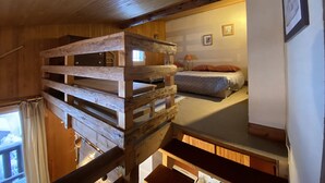 Interior rústico de una cabaña con cama en altillo, vigas de madera y una pequeña ventana.