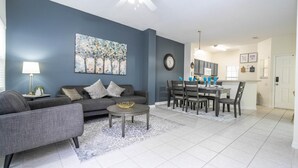 Ein modernes Wohnzimmer mit einem grauen Sofa, einem Couchtisch und einem Essbereich mit Tisch und Stühlen.