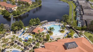 Eine Vogelperspektive zeigt einen Urlaubsort mit einem zentral gelegenen Swimmingpool, umgeben von Palmen und Liegebereichen.