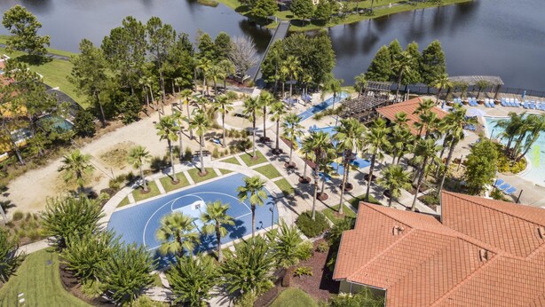 Eine Vogelperspektive zeigt ein Resort mit Basketballplatz, Palmen und einem Poolbereich.