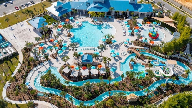 Une vue aérienne d’un complexe hôtelier doté d’une grande piscine centrale, de plusieurs petites piscines et d’un toboggan aquatique.