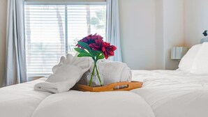 A neatly made bed with white linens, a tray with folded towels and a vase with red flowers, and a window with blinds. - Chic Vegas Retreat: Near Top Attractions (Las Vegas)