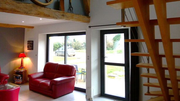 A room with a red leather sofa, a wooden ladder, and a large window with a view of the outdoors. - Charming Contemporary Farm Gîtes in Scenic Beauce Village, Private Garden & Parking (Moutiers)
