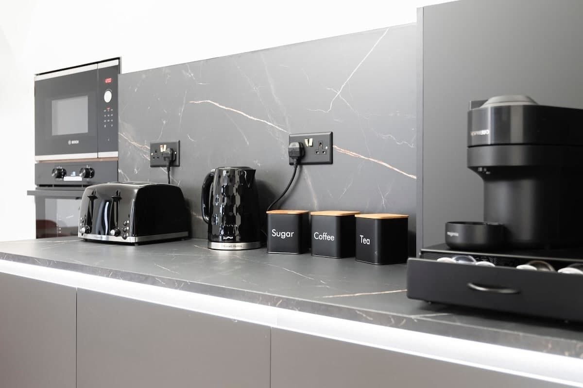 A modern kitchen with a built-in microwave, toaster, coffee maker, and storage containers for sugar, coffee, and tea.