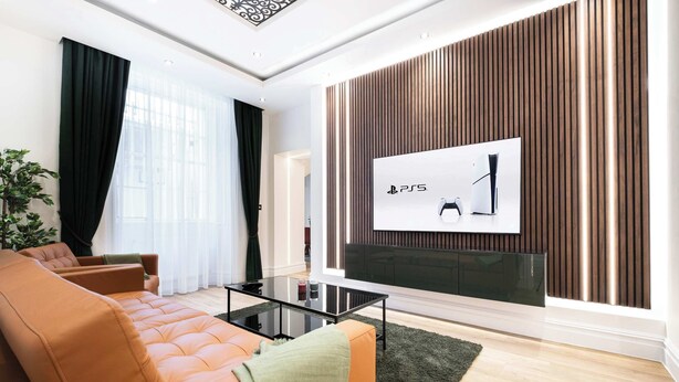 A modern living room with a sofa, a glass coffee table, a flat-screen TV mounted on a wooden wall, and a potted plant.