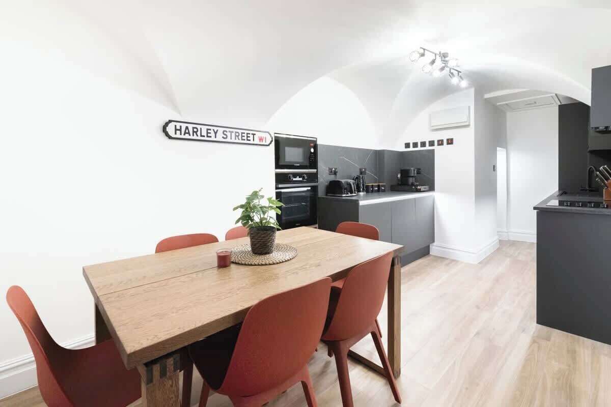 Een moderne keuken met een houten eettafel en rode stoelen, een zwarte oven en een bordje met de tekst 'HARLEY STREET W1'.