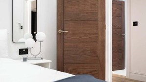 A bedroom with a wooden wardrobe, a bedside table with a lamp, and a mirror.