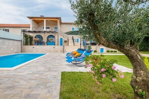 A pool area with lounge chairs, a stone patio, and a building with blue doors and columns. - Beautiful Villa Dussich in Oprtalj, Novaki (Oprtalj)