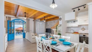 Un vaste espace de vie comprenant un coin repas avec une table pour quatre personnes, une cuisine équipée d’appareils modernes et une grande fenêtre donnant sur une cour.