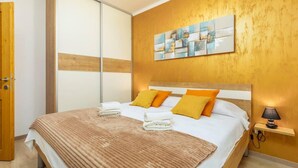 Une chambre à coucher avec un lit, des oreillers, une couverture, une table de chevet avec une lampe et une œuvre d’art murale.