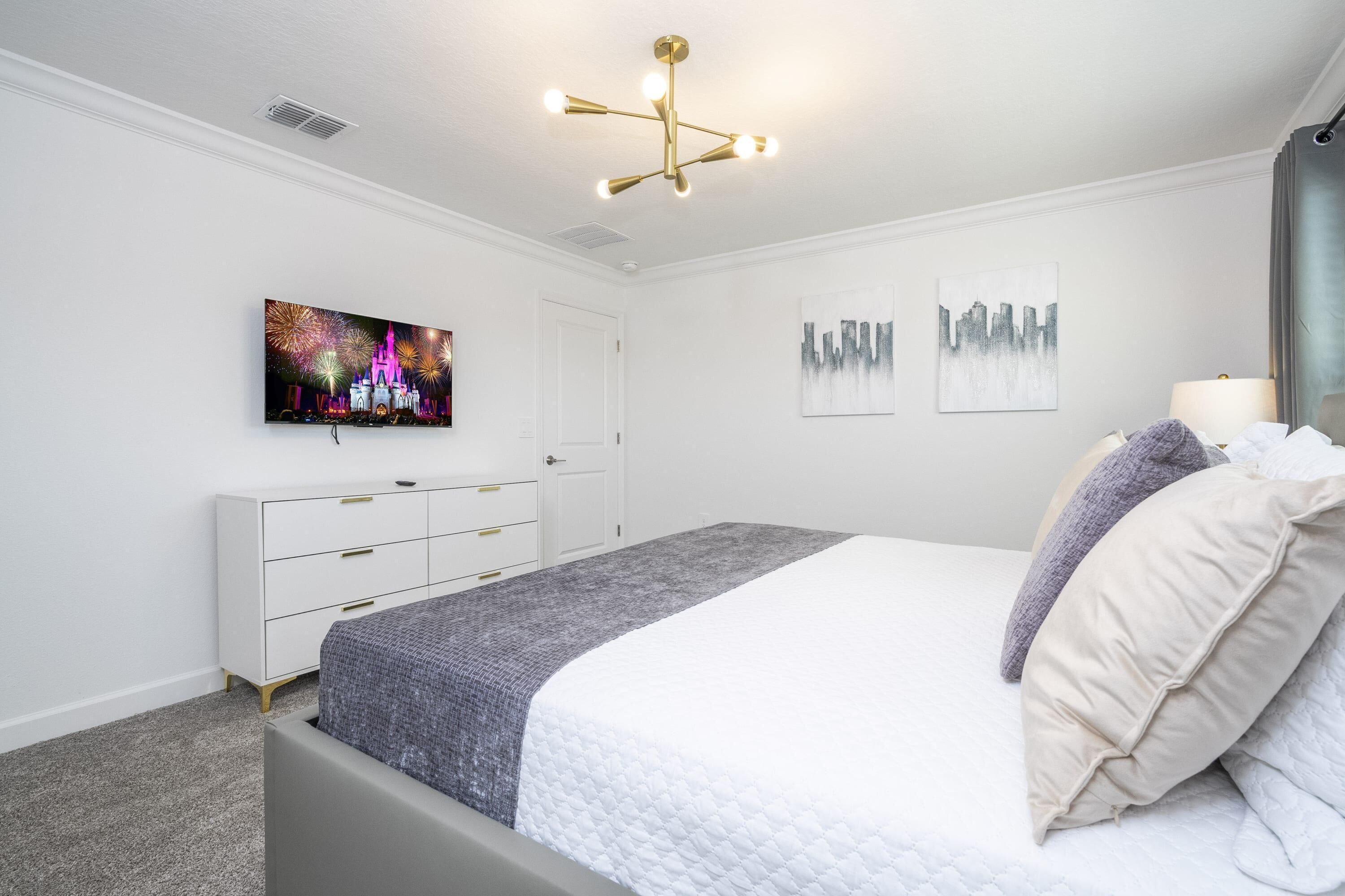Una camera da letto con un letto, una TV a parete, un comò e una lampada a soffitto.