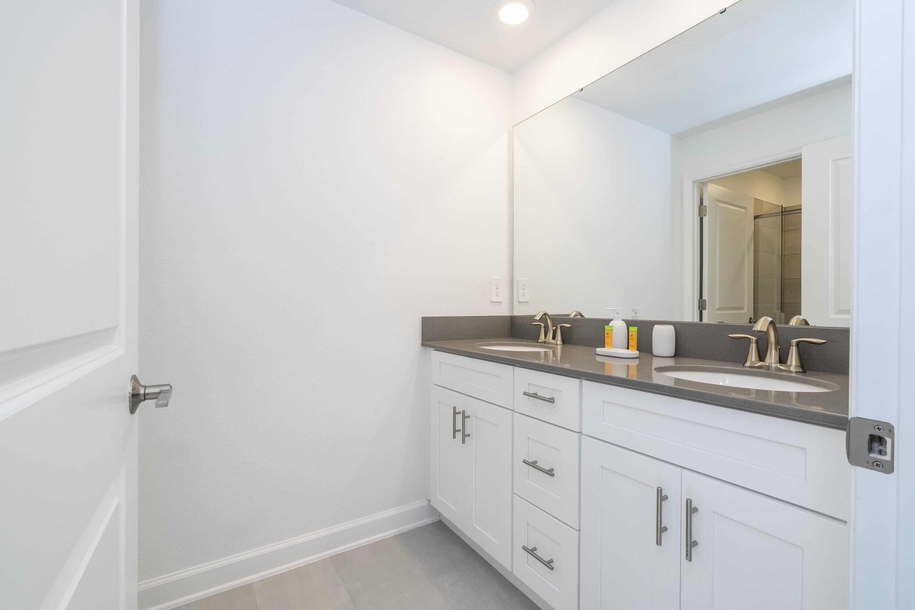 A bathroom with two sinks, a large mirror, and white cabinetry.