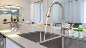 Eine moderne Küche mit einer Edelstahl-Spüle, einem eingebauten Geschirrspüler und einer Arbeitsplatte mit Obstkorb.