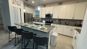 Une cuisine moderne avec des meubles blancs, des appareils en acier inoxydable et un îlot central doté de tabourets de bar.