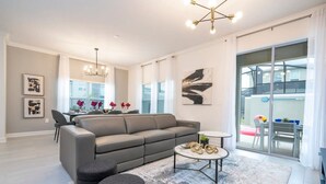 A modern living room with a grey sofa, a coffee table, and a rug. There is a dining area in the background with a table and chairs. - Stunning 4 Bd w Pool Storey Lake Resort 2400 (Kissimmee)