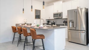 A modern kitchen with white cabinets, stainless steel appliances, and a central island with bar stools. - Stunning 4 Bd w Pool Storey Lake Resort 2400 (Kissimmee)