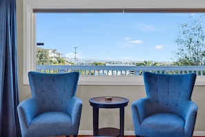 A room with two blue upholstered chairs and a small round table, a large window with a view of a cityscape and a balcony railing. - San Diego 2BD with Downtown Views, Deck & BBQ! (San Diego)