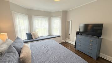 A bedroom with a bed, a bench, a dresser, a television, and a window with curtains.