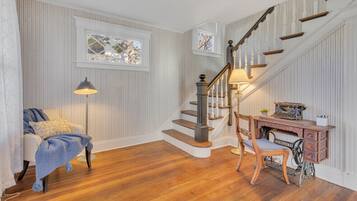 A room with a wooden staircase, a desk with a typewriter, a chair, a lamp, and a window with a view.