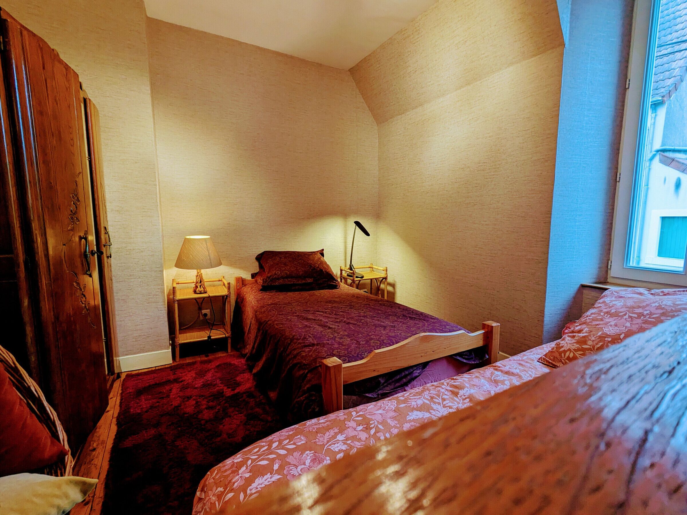 Un dormitorio con cama, mesita de noche, lámpara, una silla y un armario.